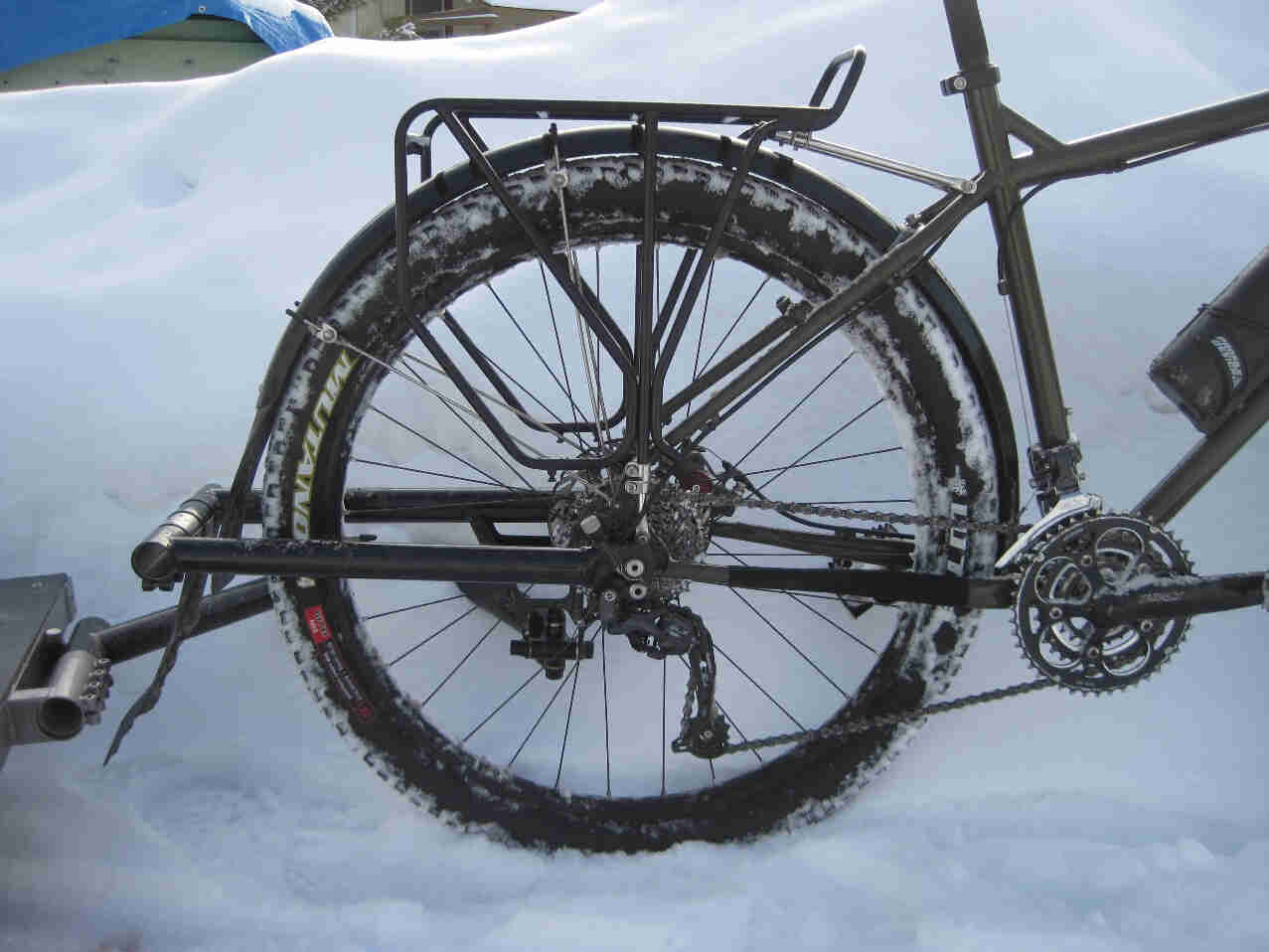 Rear side view of the rear half of a Surly Troll bike, parked against a tall snow bank